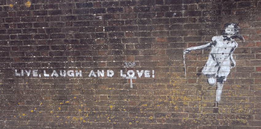 Stencil on a brick wall, depicting a girl playing  and the words 'live, laugh and love' 
